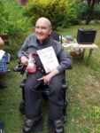 Na zdjęciu nasz Mieszkaniec na wózku elektrycznym trzymający w ręku dyplom i wygraną